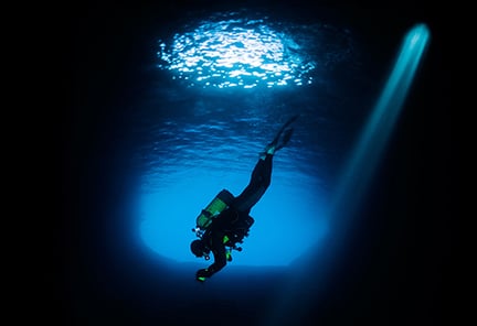 A scuba diver diving deeper into the depths of a dark sea, with light shining behind them, much like entering the deep web or the dark web.